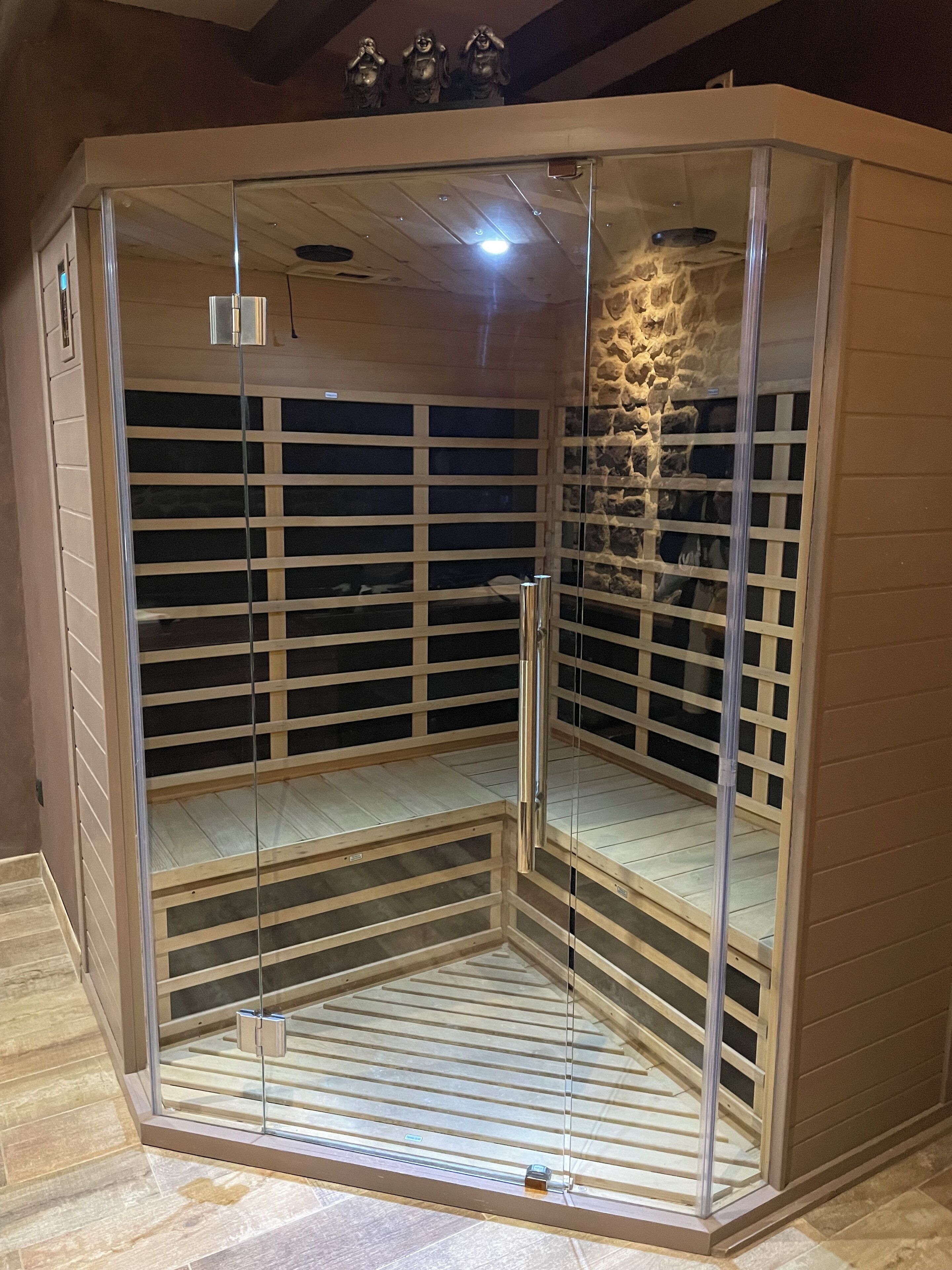 Un sauna aux murs de verre, doté d’un banc en bois et d’un mur en pierre.