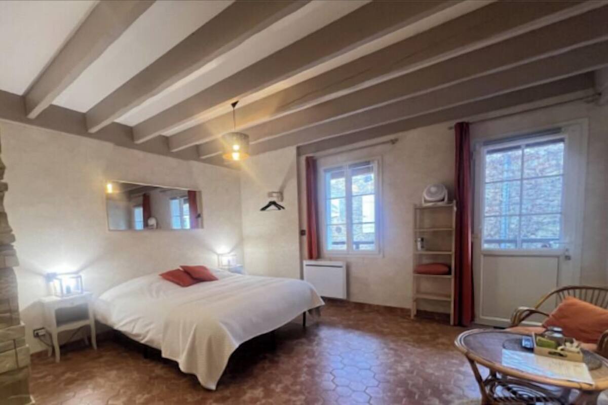 Ein Schlafzimmer mit Bett, Nachttisch, Spiegel, Fenster und einem Sessel.