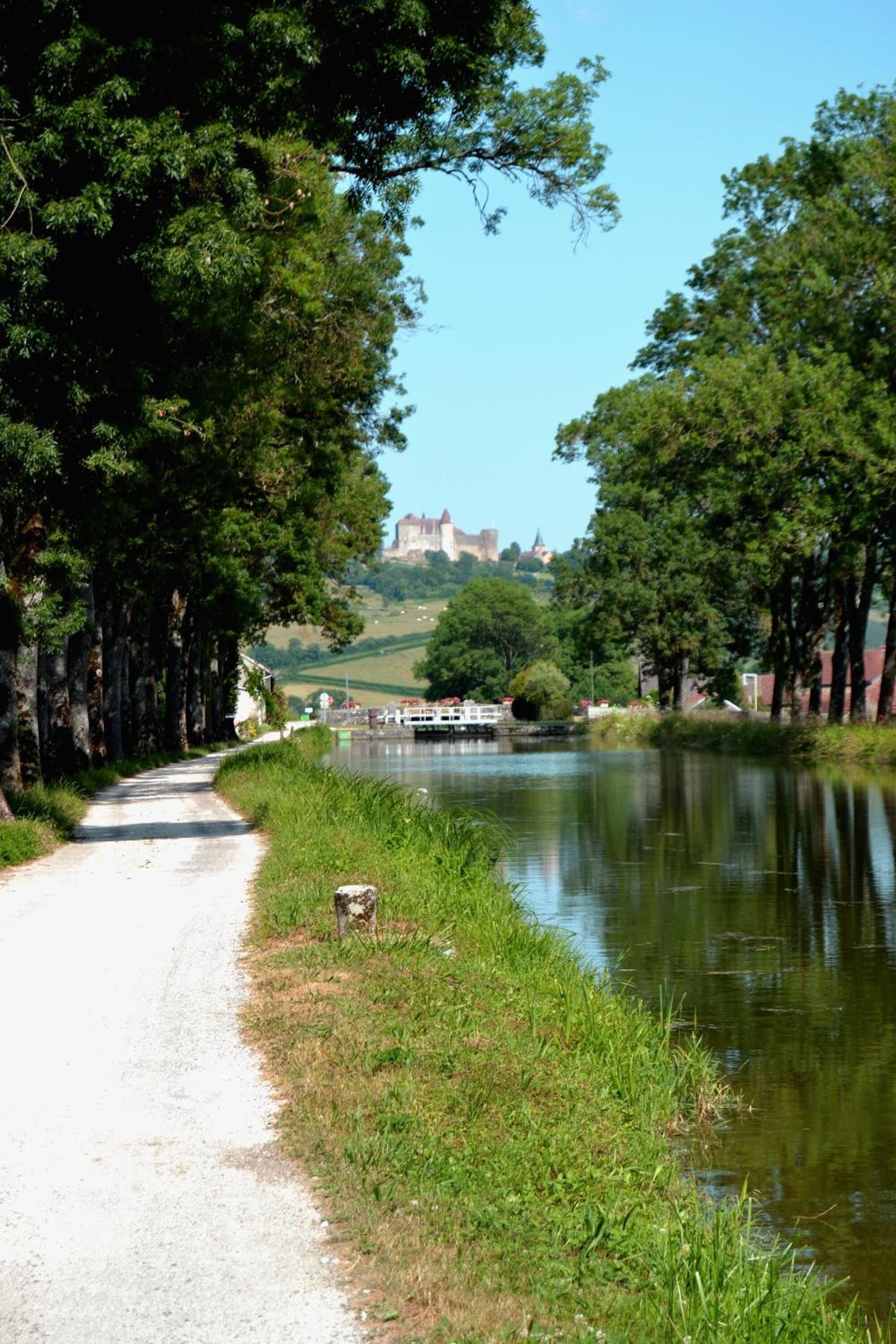 A pathway beside a calm river with a castle in the distance.