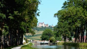 A pathway beside a calm river with a castle in the distance.