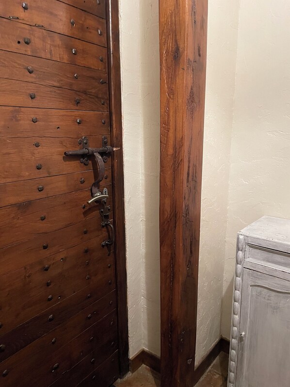 Una puerta de madera con herrajes metálicos, un poste de madera y una pared blanca.
