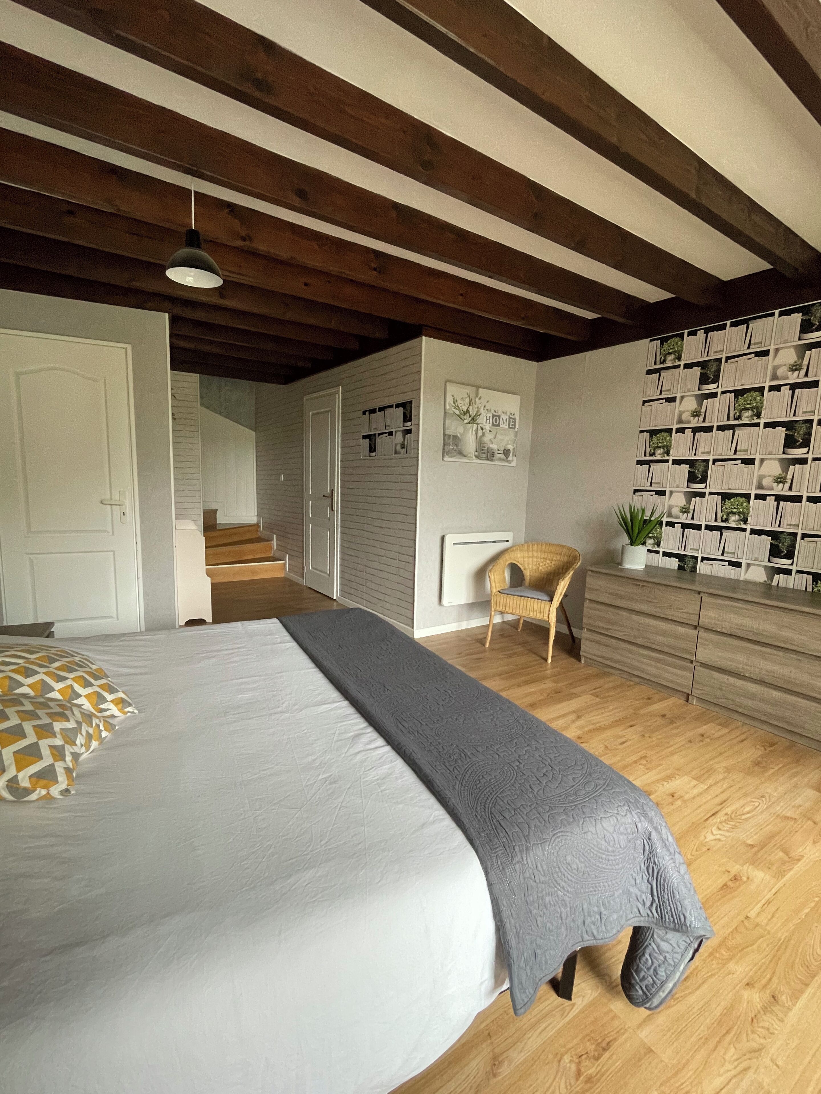 Un dormitorio con una cama grande, piso de madera, una escalera que conduce a un nivel superior y un muro con estanterías empotradas.