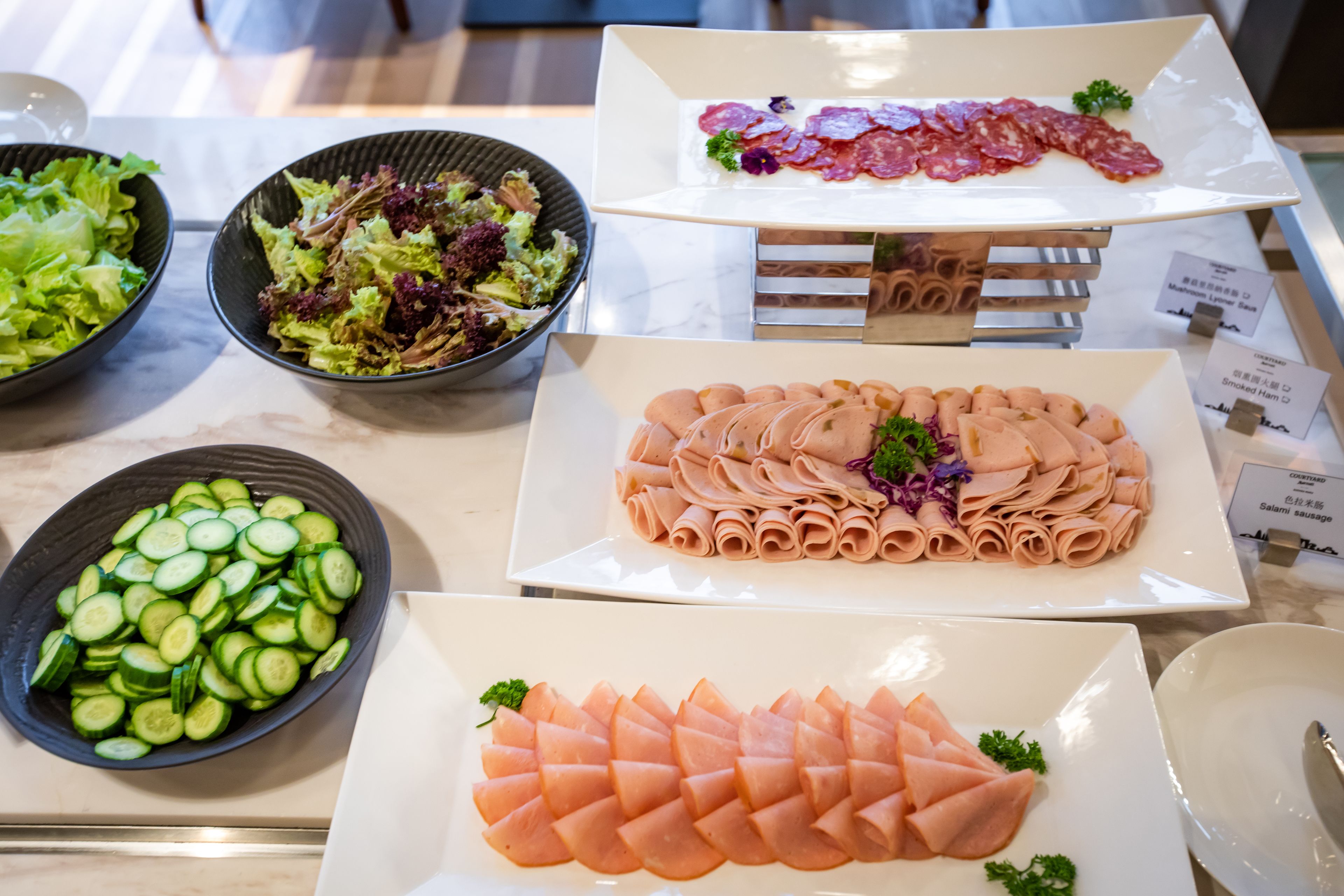 Une table de buffet proposant divers plats, notamment des tranches de concombre, une salade et différents types de viande.