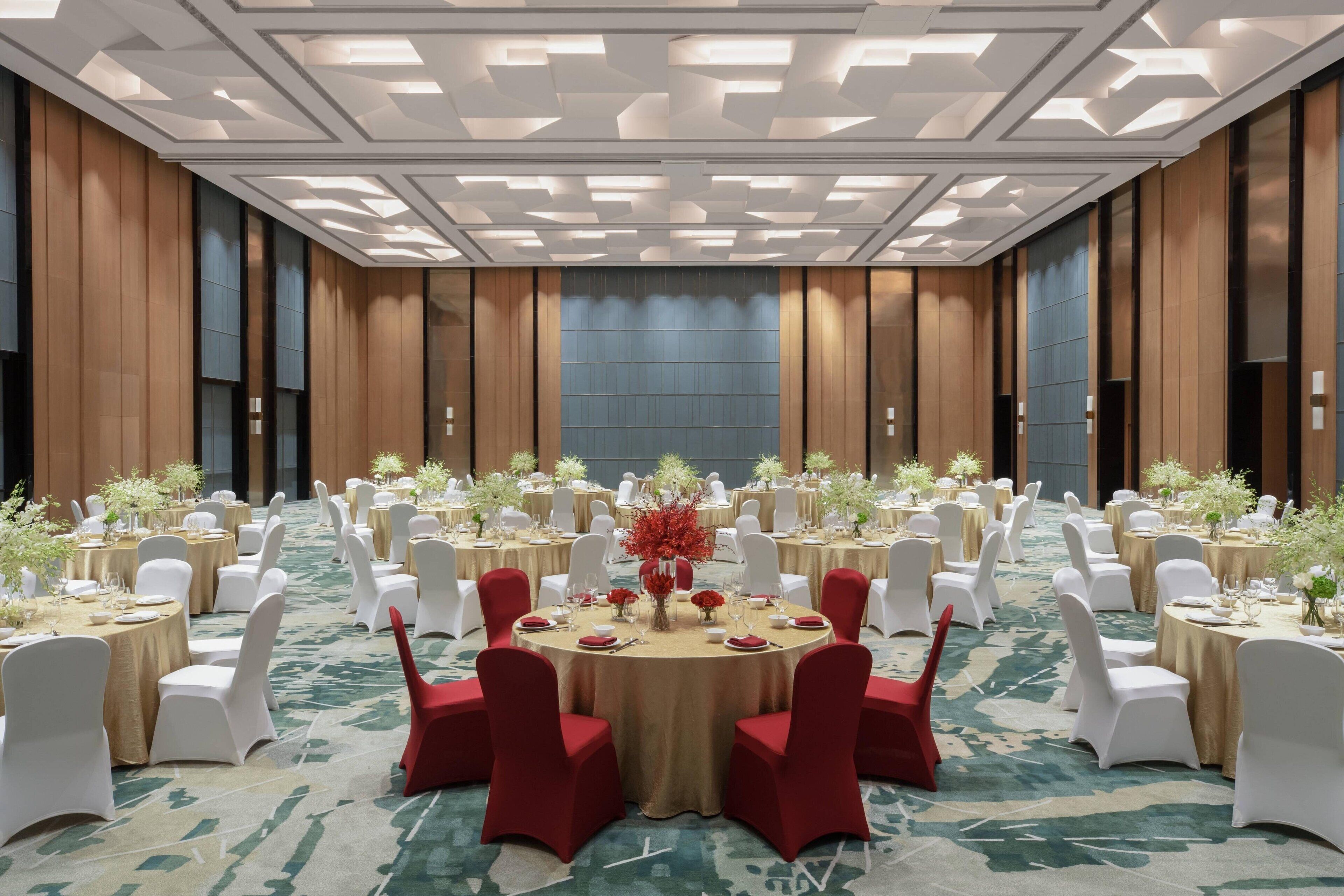Un salón de banquetes con mesas redondas, sillas blancas y rojas, y centros de mesa florales.