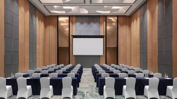 A conference room with rows of tables, white chairs, and a projector screen.