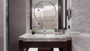 Un baño moderno con un lavabo de mármol, un espejo grande y un mueble de tocador de madera oscura.