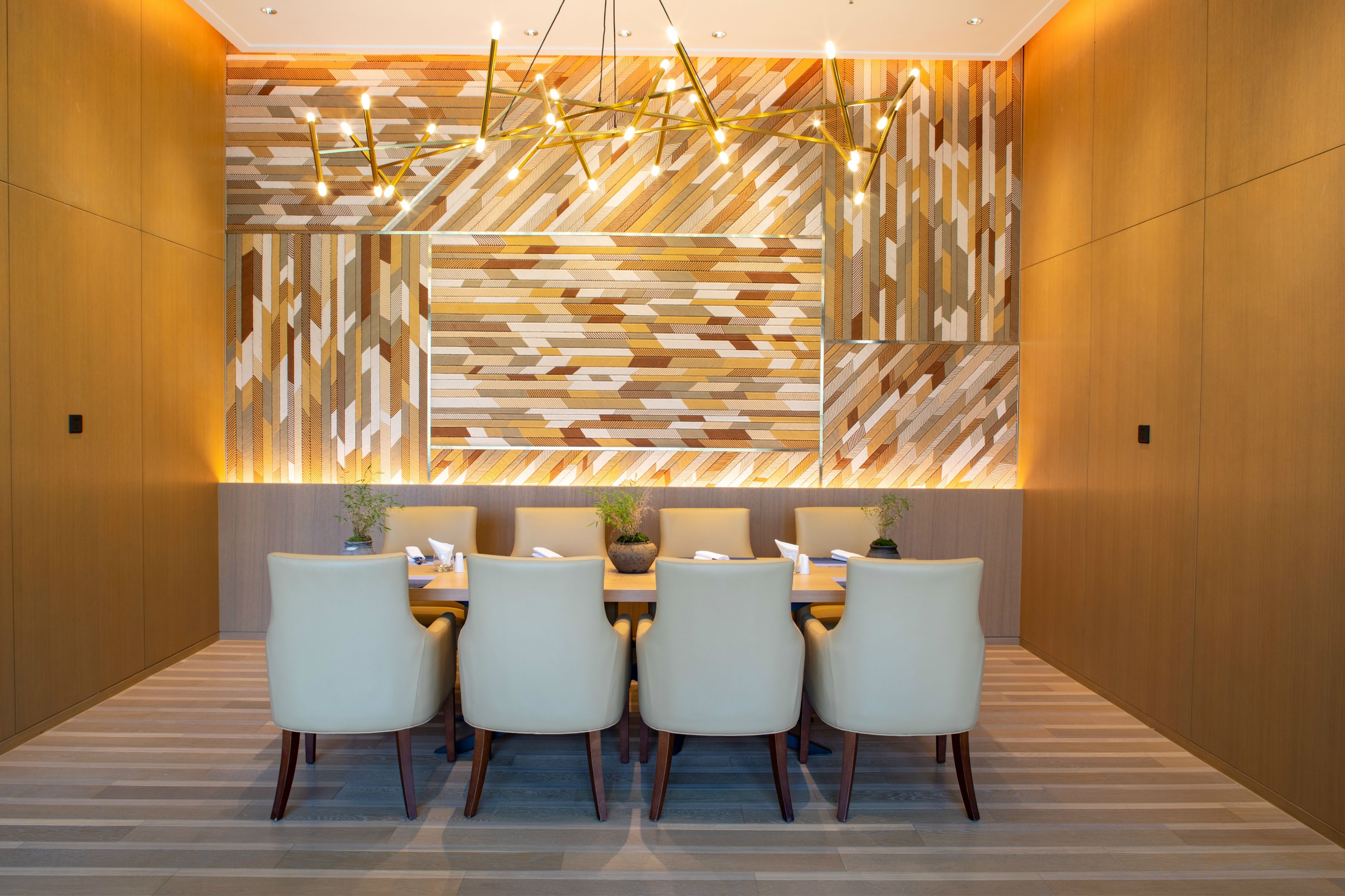 A modern dining area with a geometric patterned wall, a wooden floor, and a chandelier.