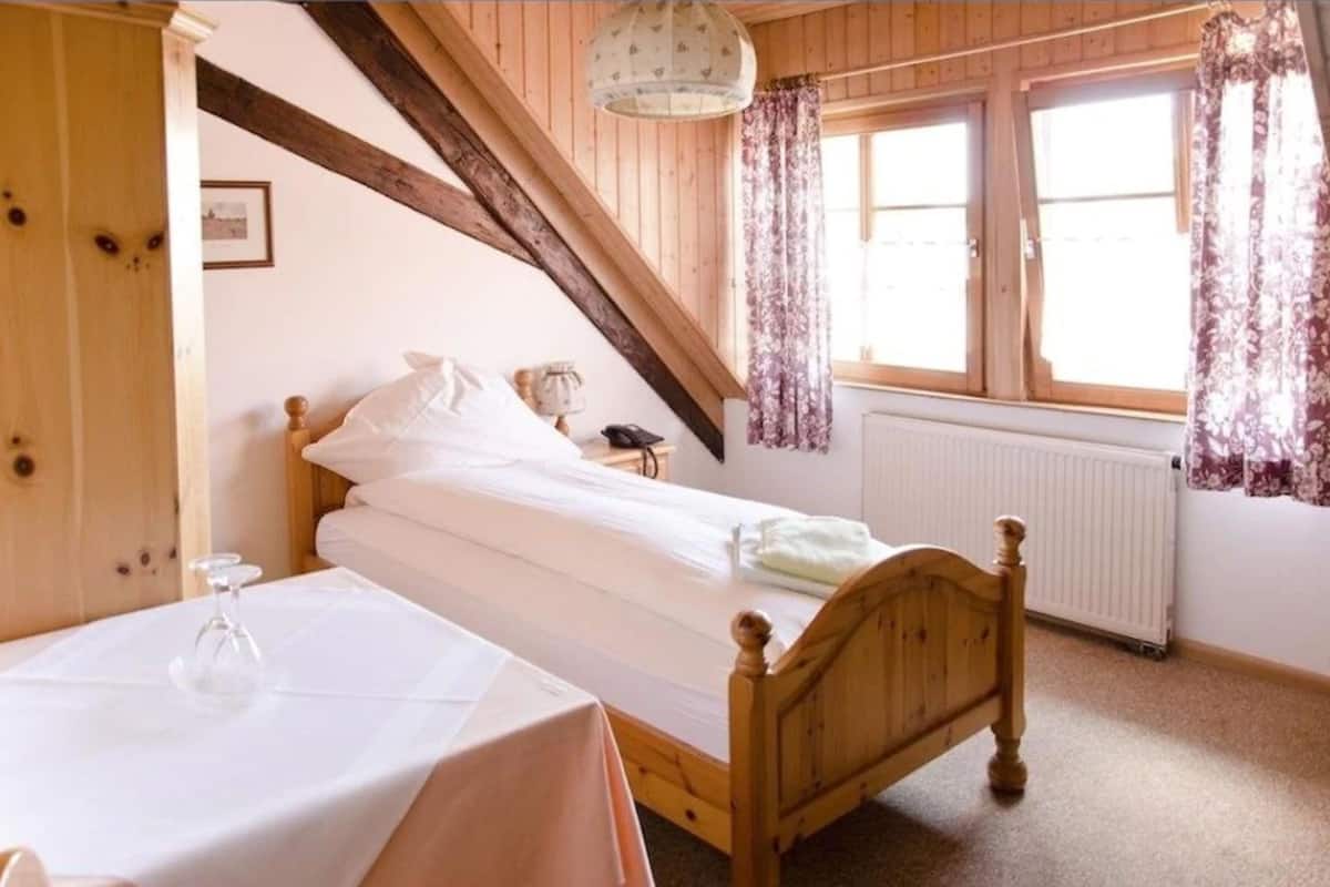 Un dormitorio con una cama de madera, una mesa con un vaso y una ventana con cortinas.
