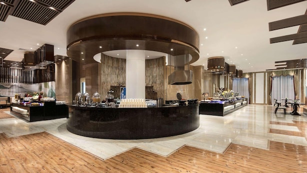 Un moderno vestíbulo de hotel con un mostrador de recepción central, piso de madera y un techo alto con iluminación empotrada.