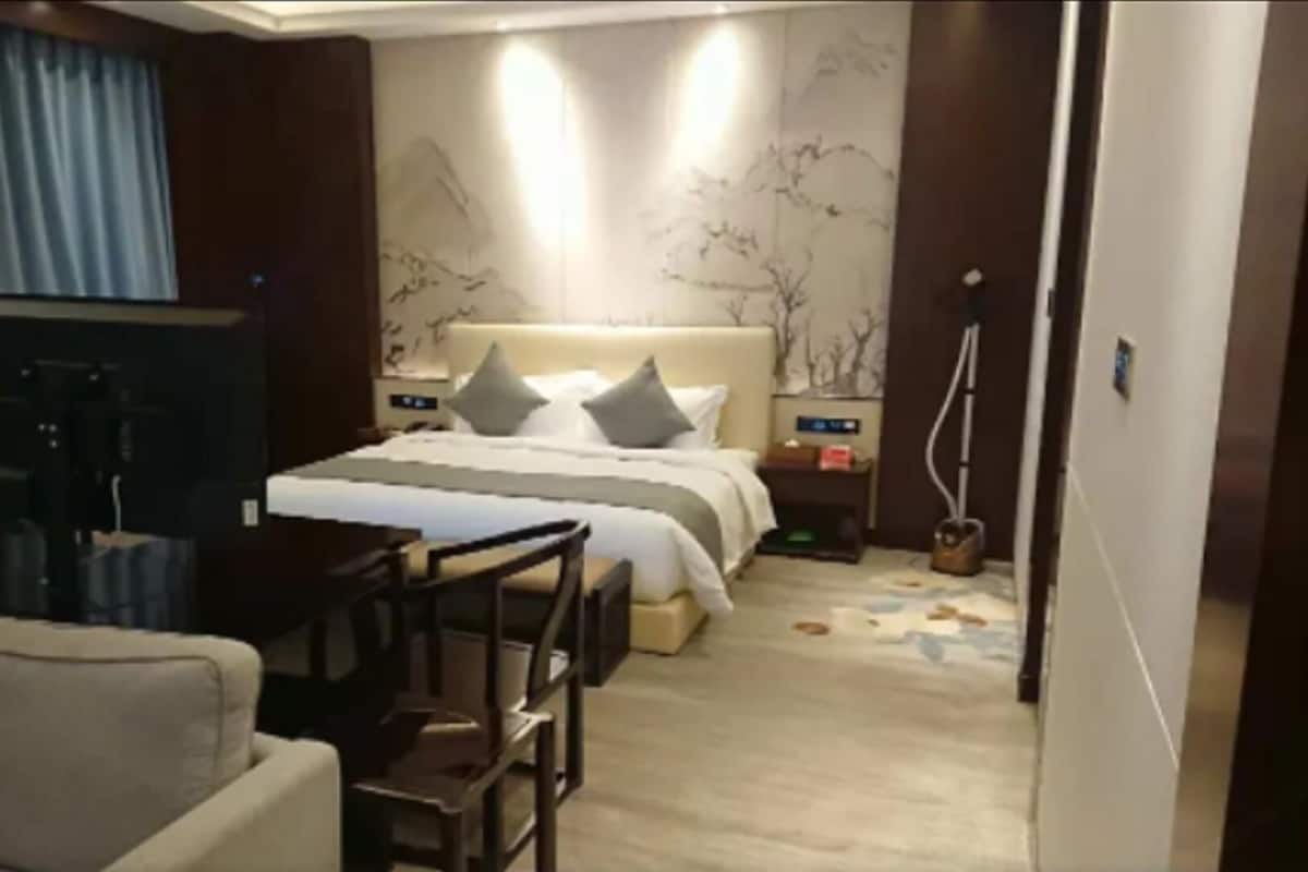 Habitació d'hotel amb llit, escriptori, cadira, televisió i una finestra gran amb cortines.