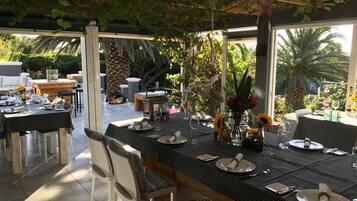 An outdoor dining area with tables set for two, surrounded by greenery and palm trees.