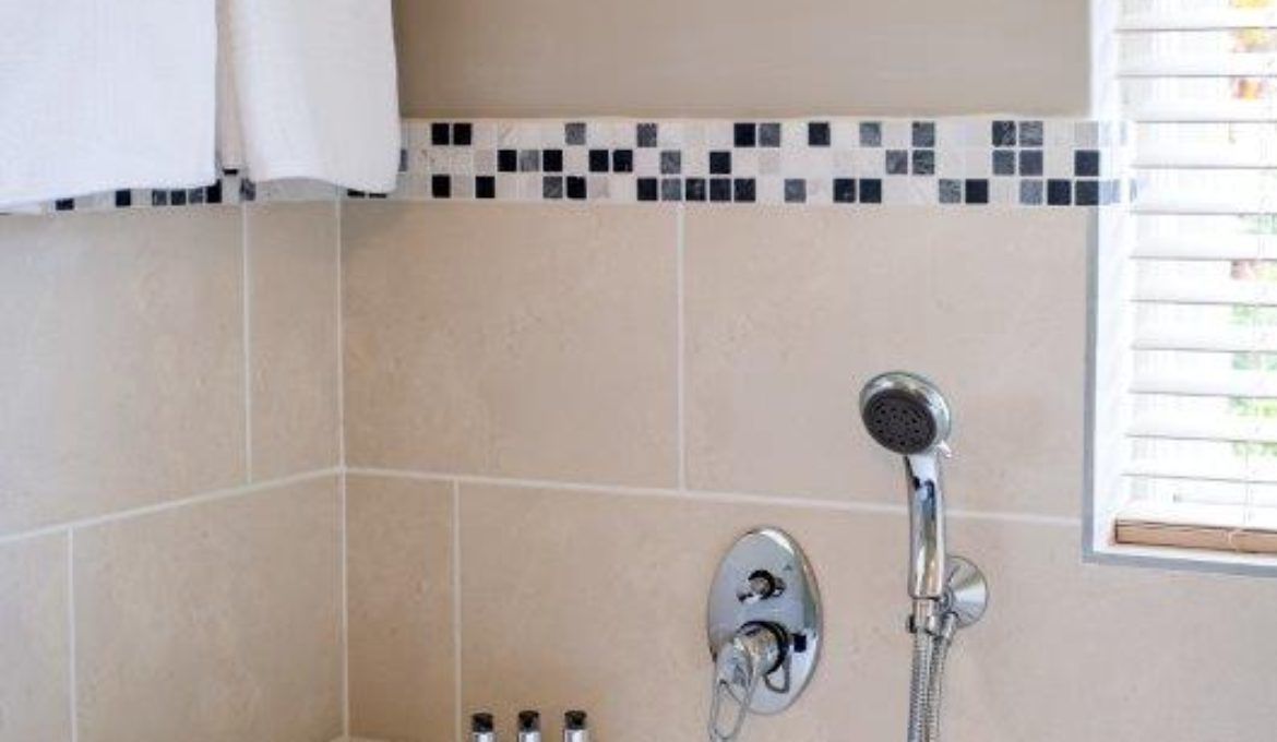 Une salle de bain avec des carreaux de couleur beige, une pomme de douche et une fenêtre avec des stores.