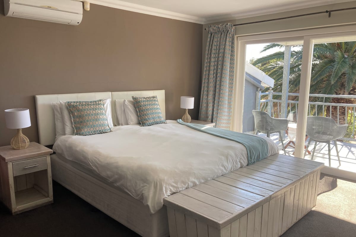 Une chambre à coucher avec un grand lit, une table de chevet avec une lampe, et une vue sur l’extérieur grâce à une porte-fenêtre coulissante.