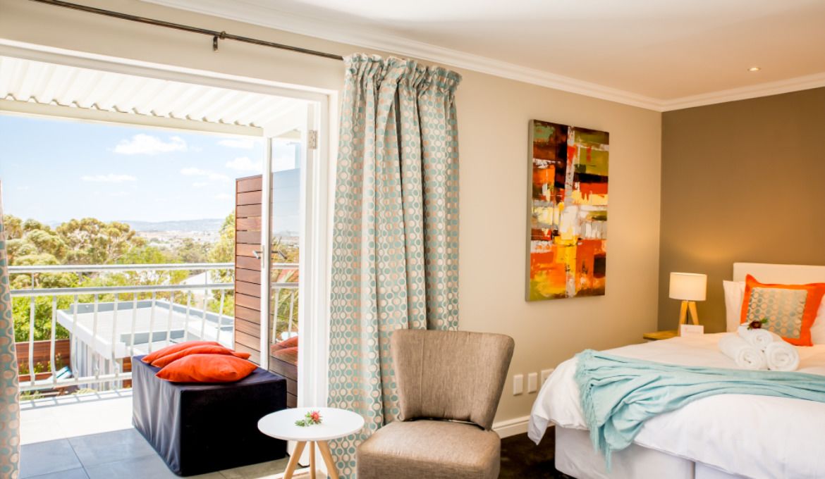 Habitación de hotel con cama, una silla, una mesita y un balcón con vistas.