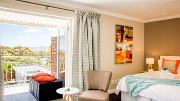 Habitación de hotel con cama, una silla, una mesita y un balcón con vistas.