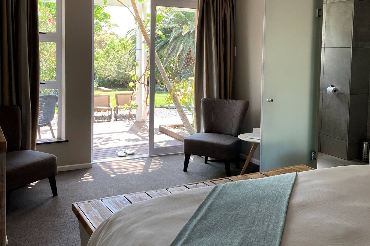 Une chambre d’hôtel comprenant un lit, une chaise, une petite table et une porte-fenêtre coulissante donnant sur un espace extérieur.
