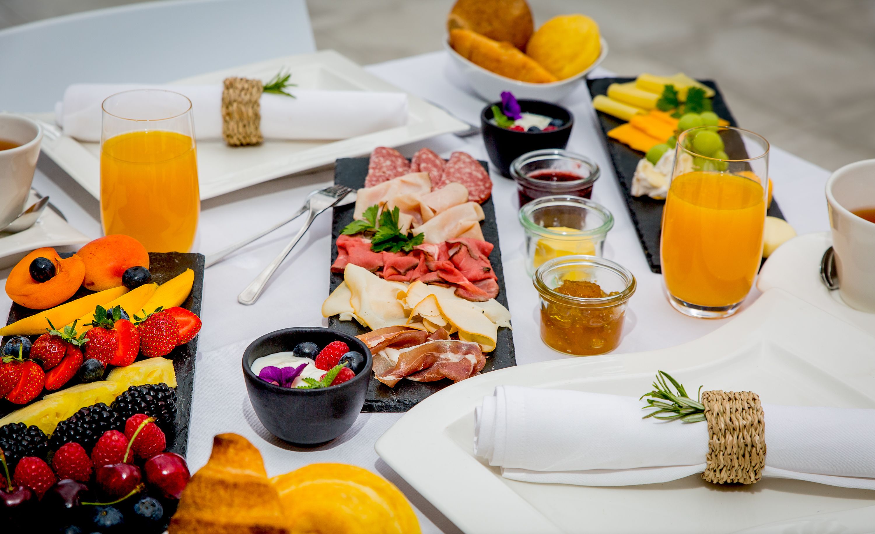 Un bufé de desayuno con frutas, quesos, embutidos y bebidas variadas.