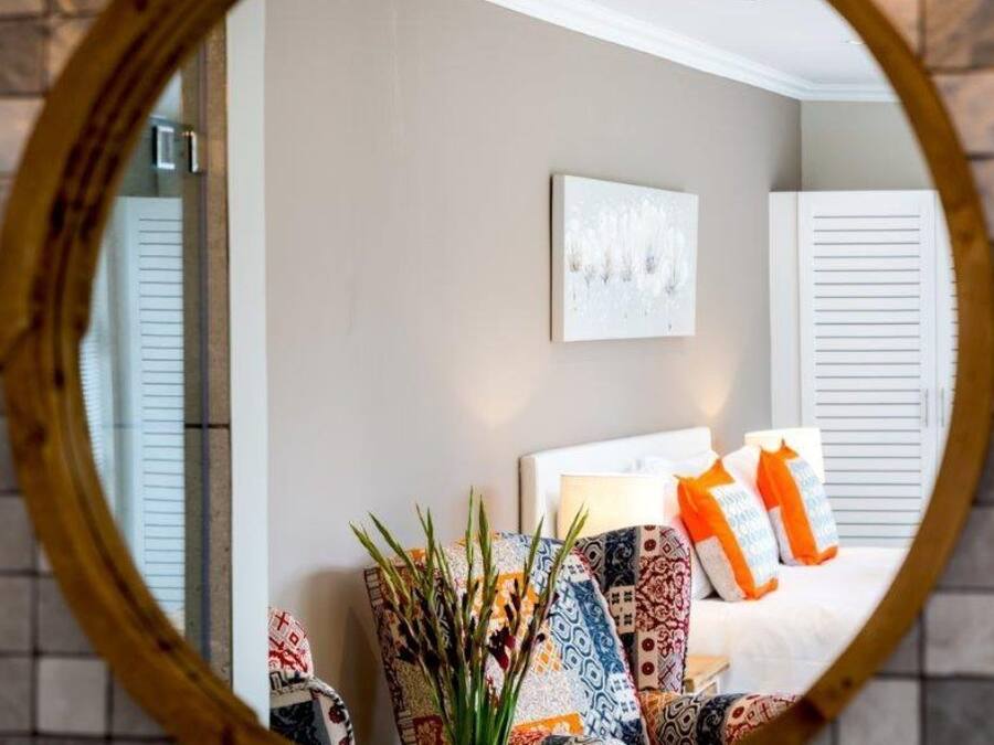 A bedroom with a bed, pillows, a mirror, and a wall-mounted artwork.