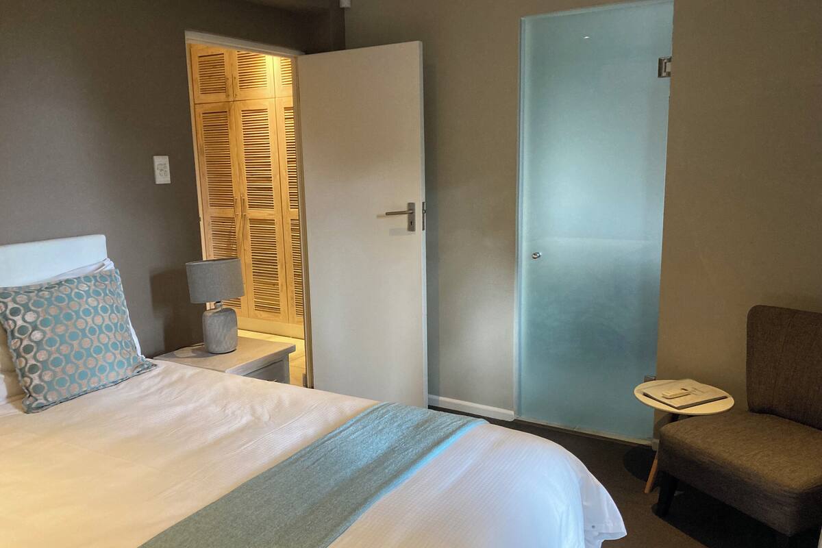 Une chambre d’hôtel comprenant un lit, une chaise, une table de chevet, une lampe et une armoire avec un miroir.
