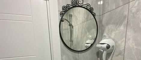A bathroom with a white door, a round mirror, a white sink, and a handheld showerhead.