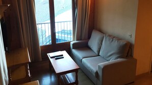 A room with a sofa, a small table, and a window with curtains. - Apartamentos  Sherpa (Pas de la Casa)