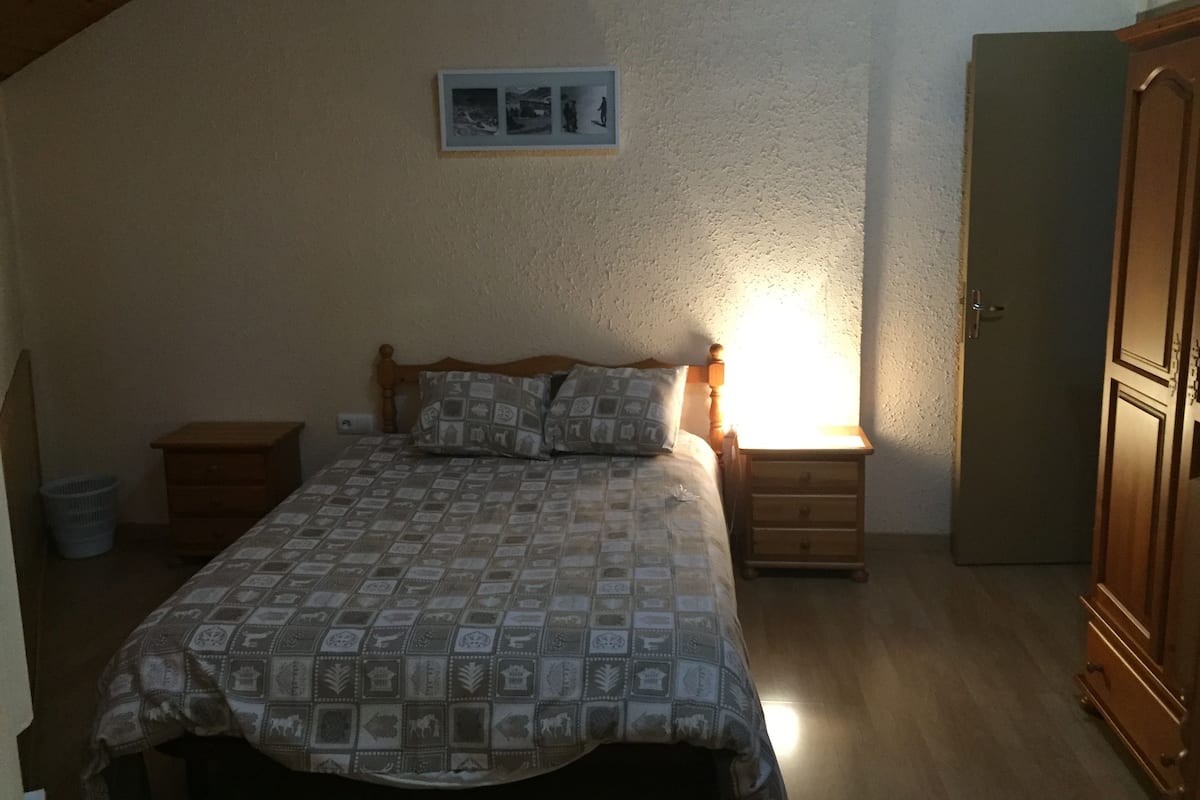 A bedroom with a bed, nightstands, a wooden wardrobe, and a wall-mounted picture.