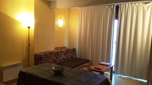 A room with a dining table, chairs, a sofa, a lamp, and a window with curtains. - Apartamentos  Sherpa (Pas de la Casa)