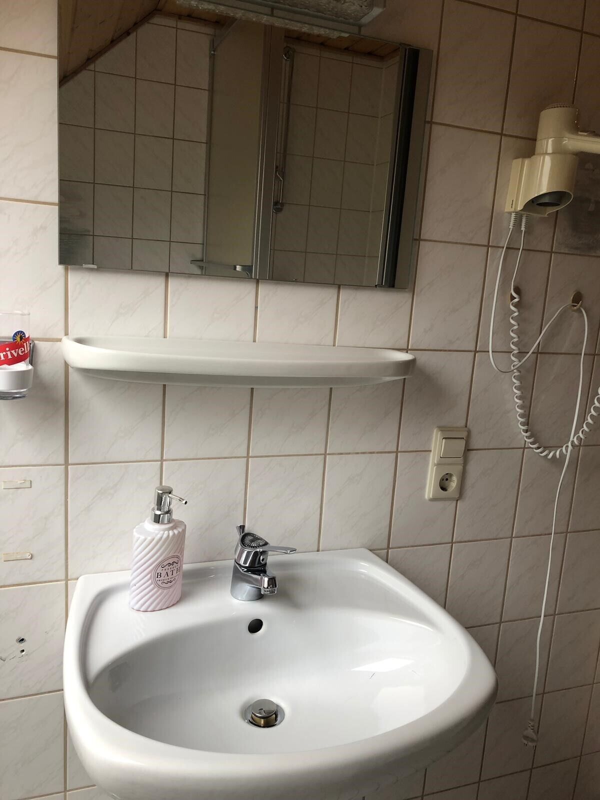 Casa de banho com uma pia branca, um espelho em cima, um porta-toalhas e uma cabine de duche com chuveiro manual.