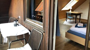 A cozy attic bedroom with a bed, a small desk, and a window overlooking a house. - Sporthostel Rössle (Schluchsee)