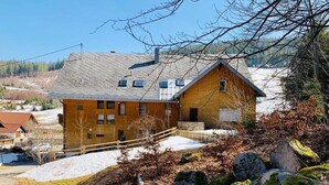 A rustic wooden house with a sloped roof, a stone foundation, and a small porch. - Sporthostel Rössle (Schluchsee)