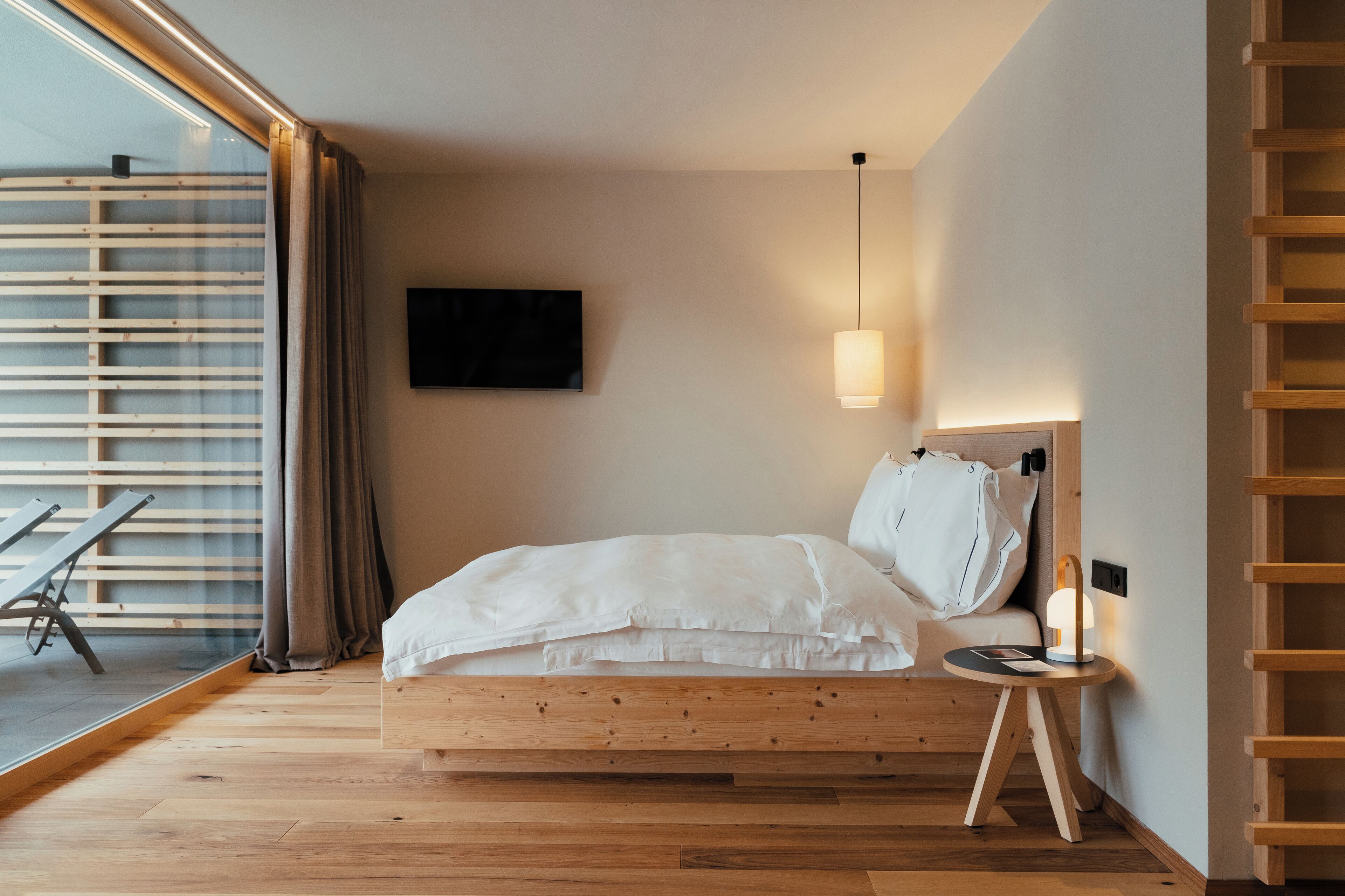Un dormitorio con una cama de madera, una mesita de noche, un televisor y un ventanal con persianas.