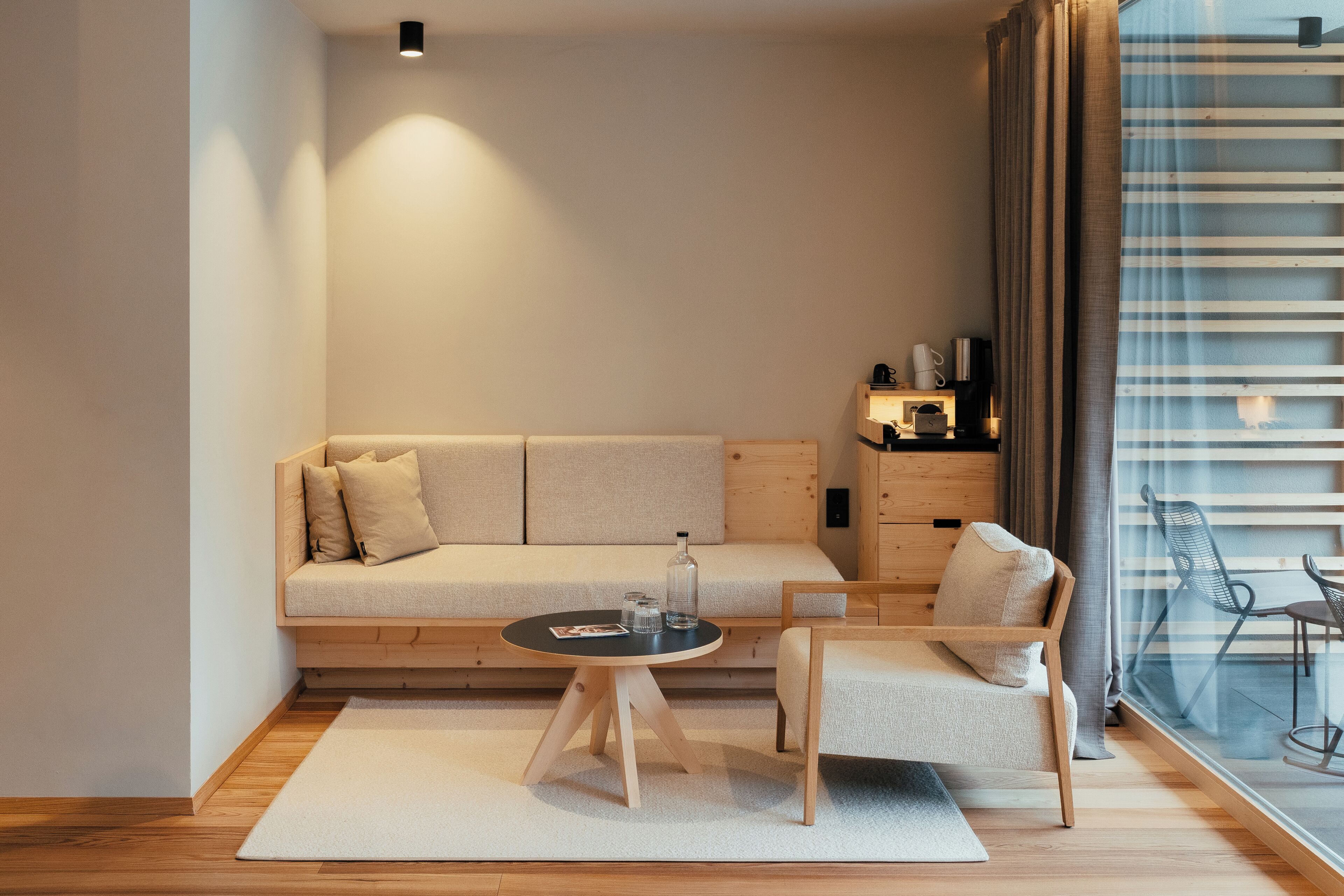 A modern living room with a sofa, a small round table, a chair, and a view through a window with curtains.