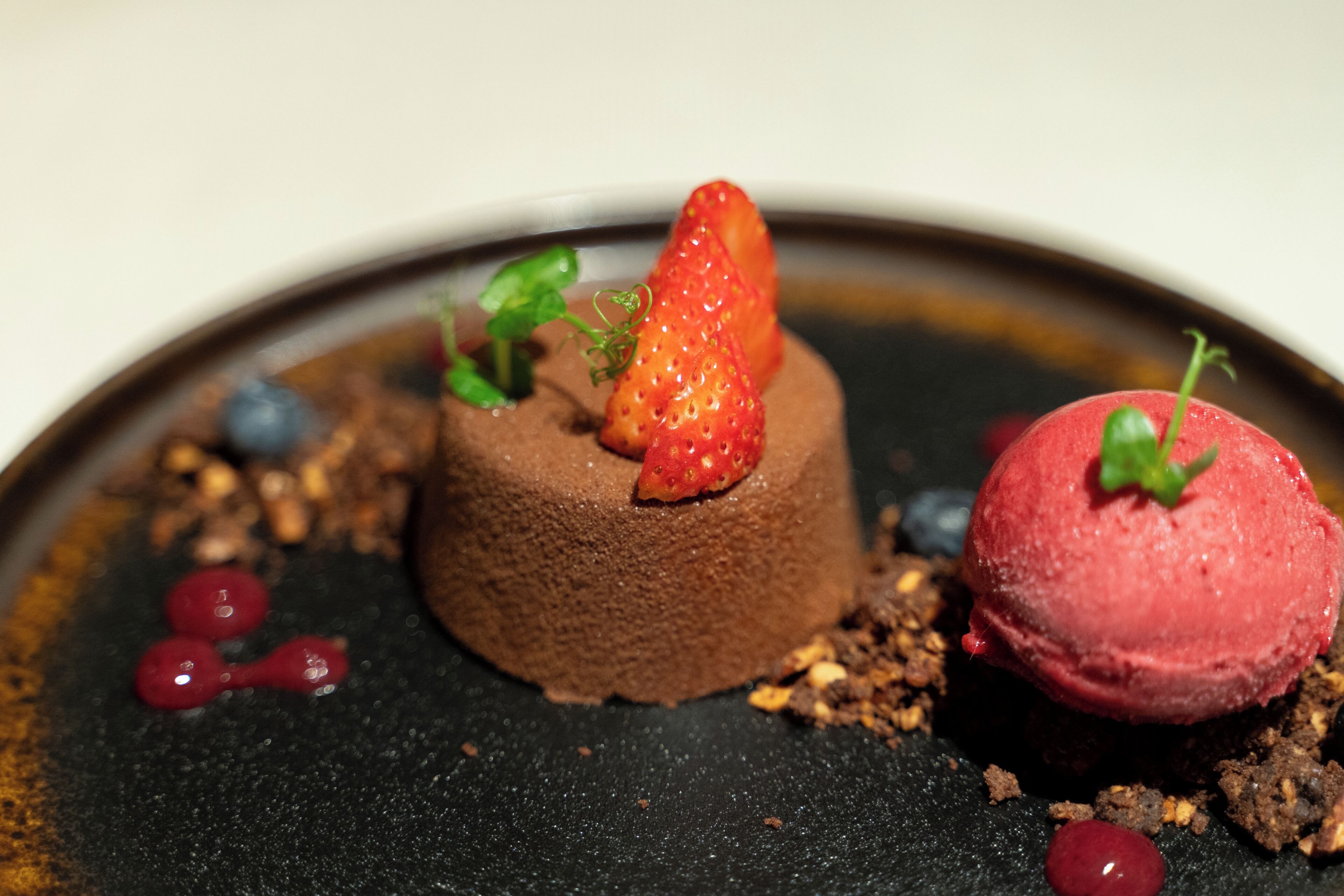 A dessert with chocolate mousse, strawberries, and a scoop of red ice cream on a plate.