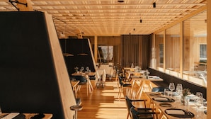 A restaurant with wooden ceiling beams, long dining tables, and chairs. - Sensoria Dolomites (Castelrotto)