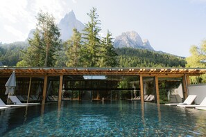 An outdoor swimming pool with lounge chairs and a pergola, surrounded by trees and mountains. - Sensoria Dolomites (Castelrotto)