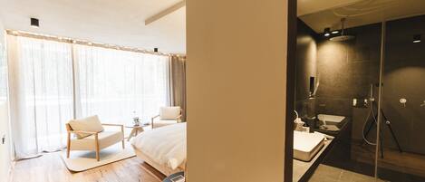 A bedroom with a bed, two chairs, a small table, and a large window with curtains.