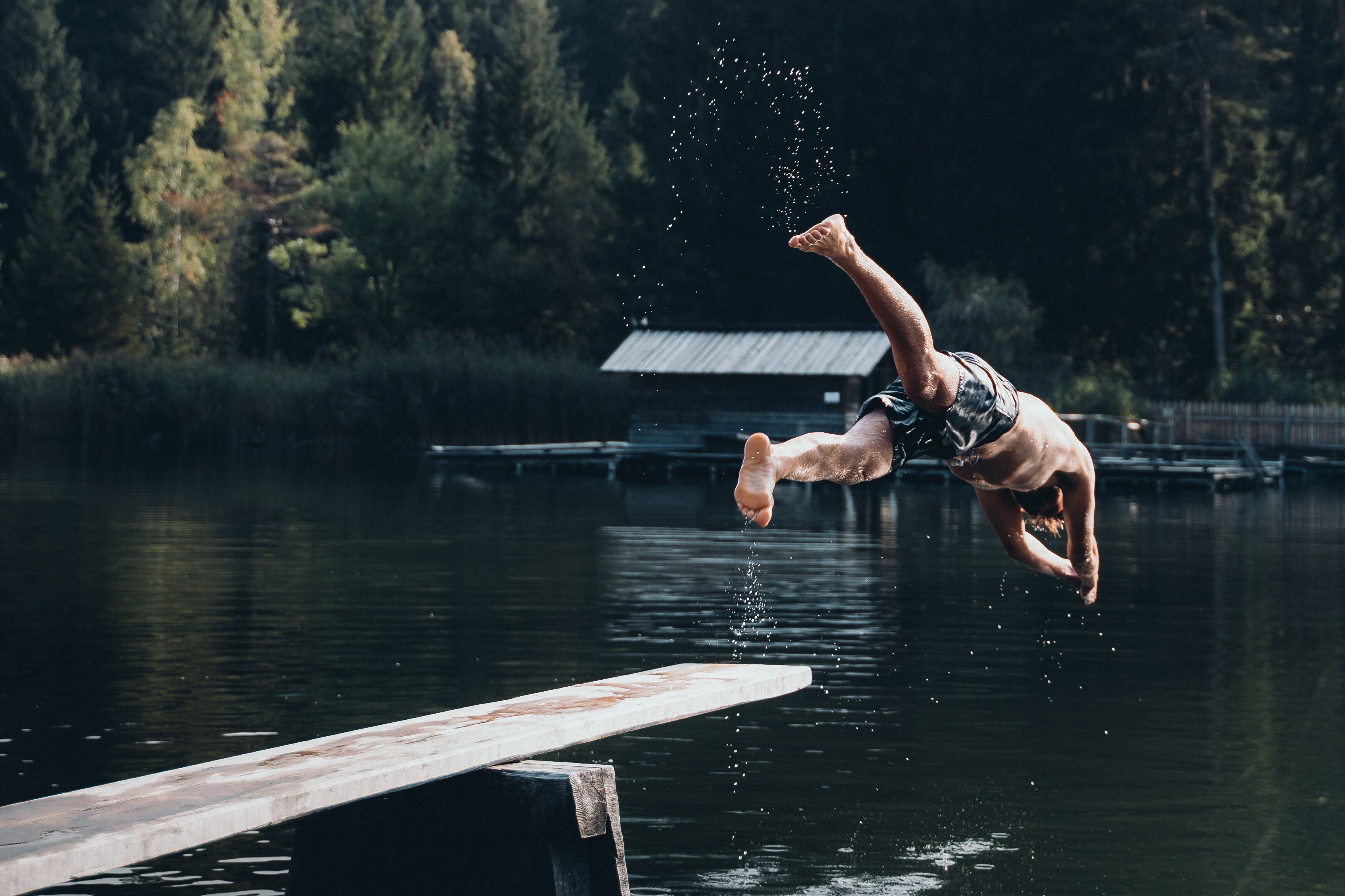 A person diving off a dock into a lake surrounded by trees.