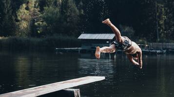 A person diving off a dock into a lake surrounded by trees.