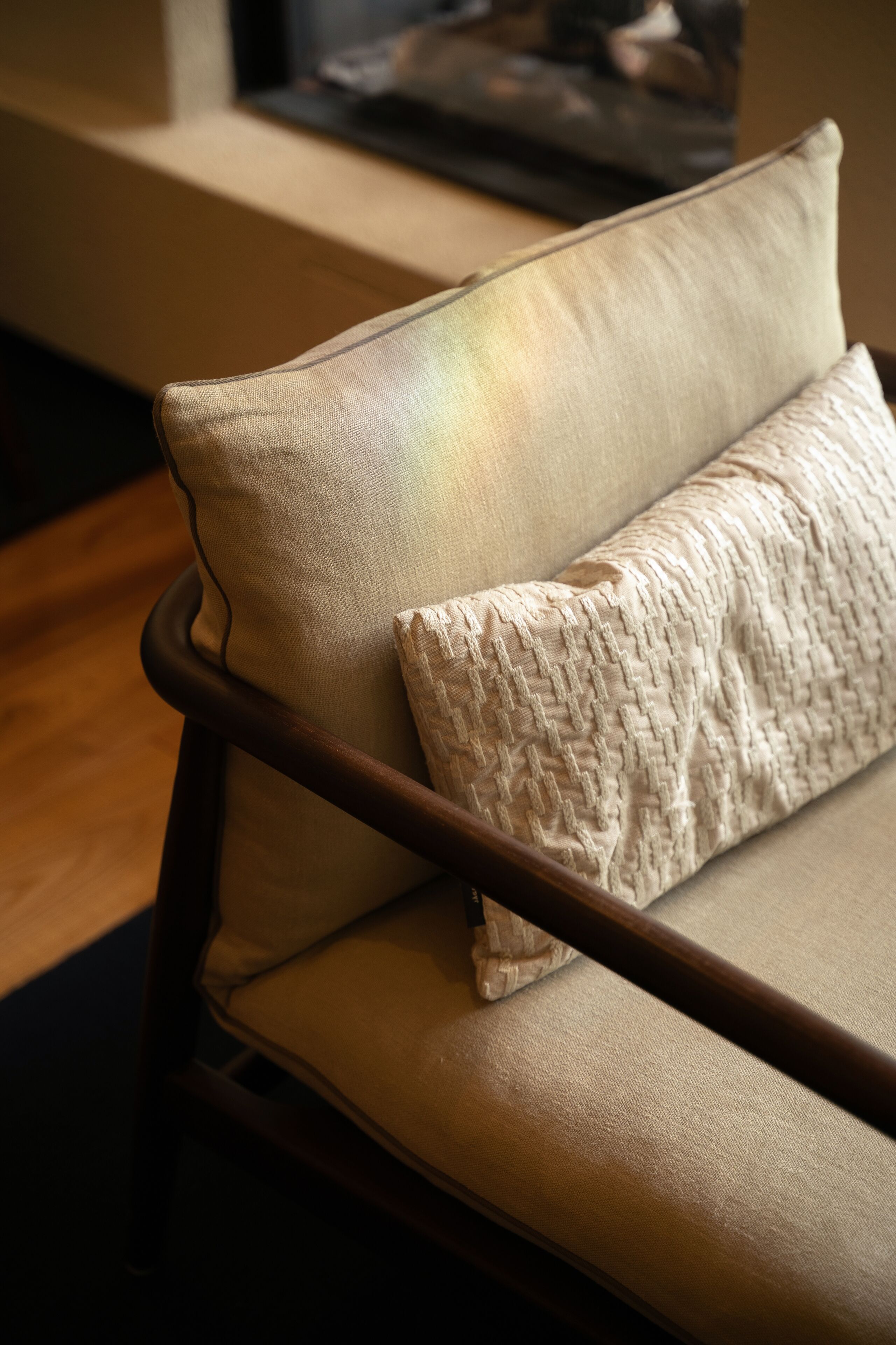 A sofa with a cushion, wooden armrests, and a wooden floor.