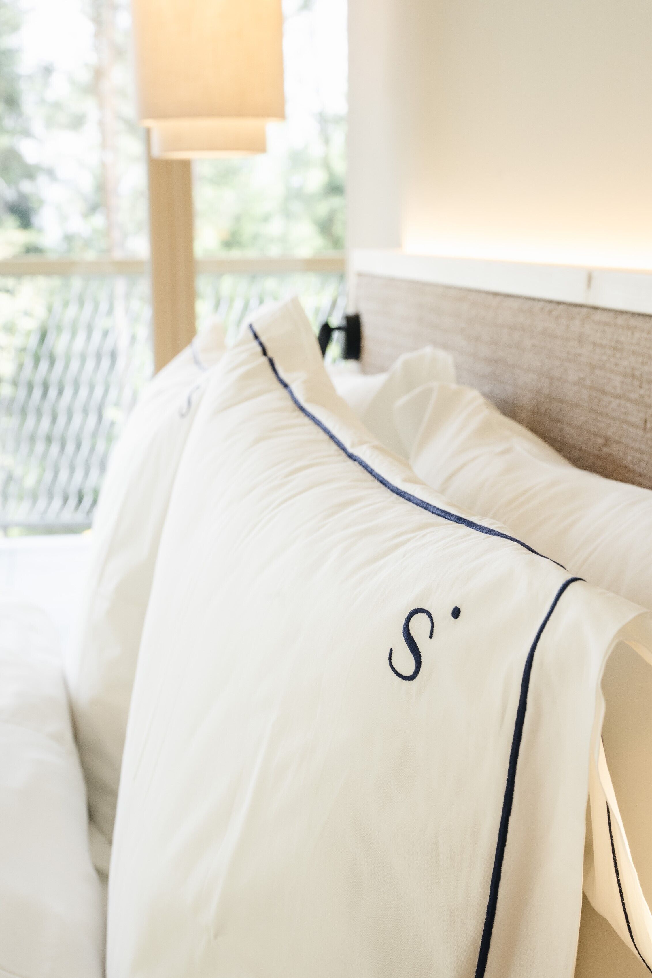 En pænt redt seng med hvide sengetæpper og en pude med et monogram.