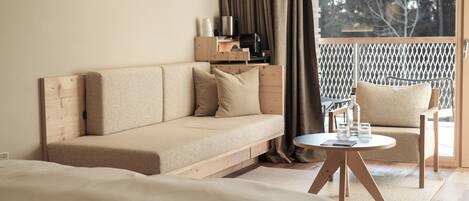 A modern hotel room with a sofa, a small round table with glasses, a chair, and a balcony with a lattice railing.