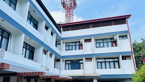 Um edifício com vários andares, teto plano, janelas grandes e uma área de entrada coberta com plantas em vasos.