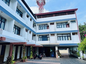 A multi-story building with a flat roof, large windows, and a covered entrance area with potted plants. - Subhas Hotel (Jaffna)