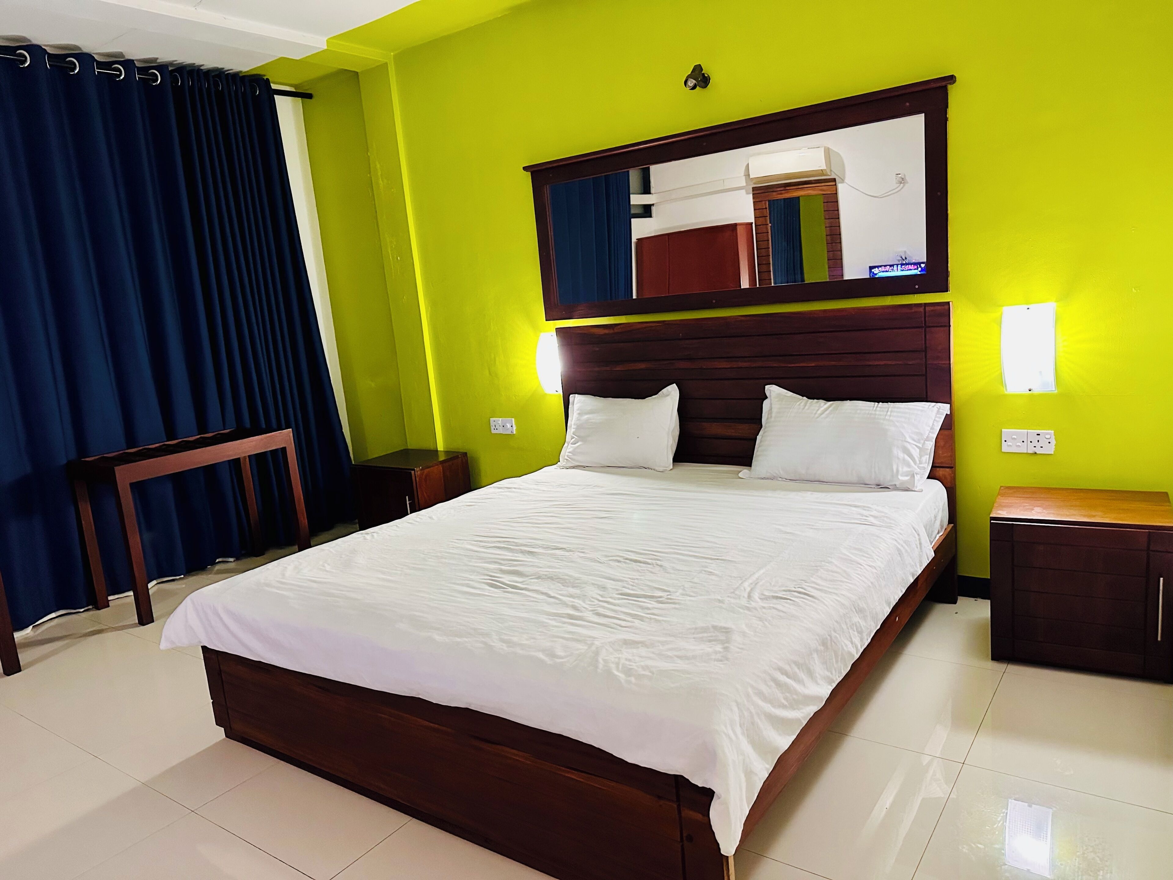 A hotel room with a bed, a nightstand, a mirror, and a window with curtains.
