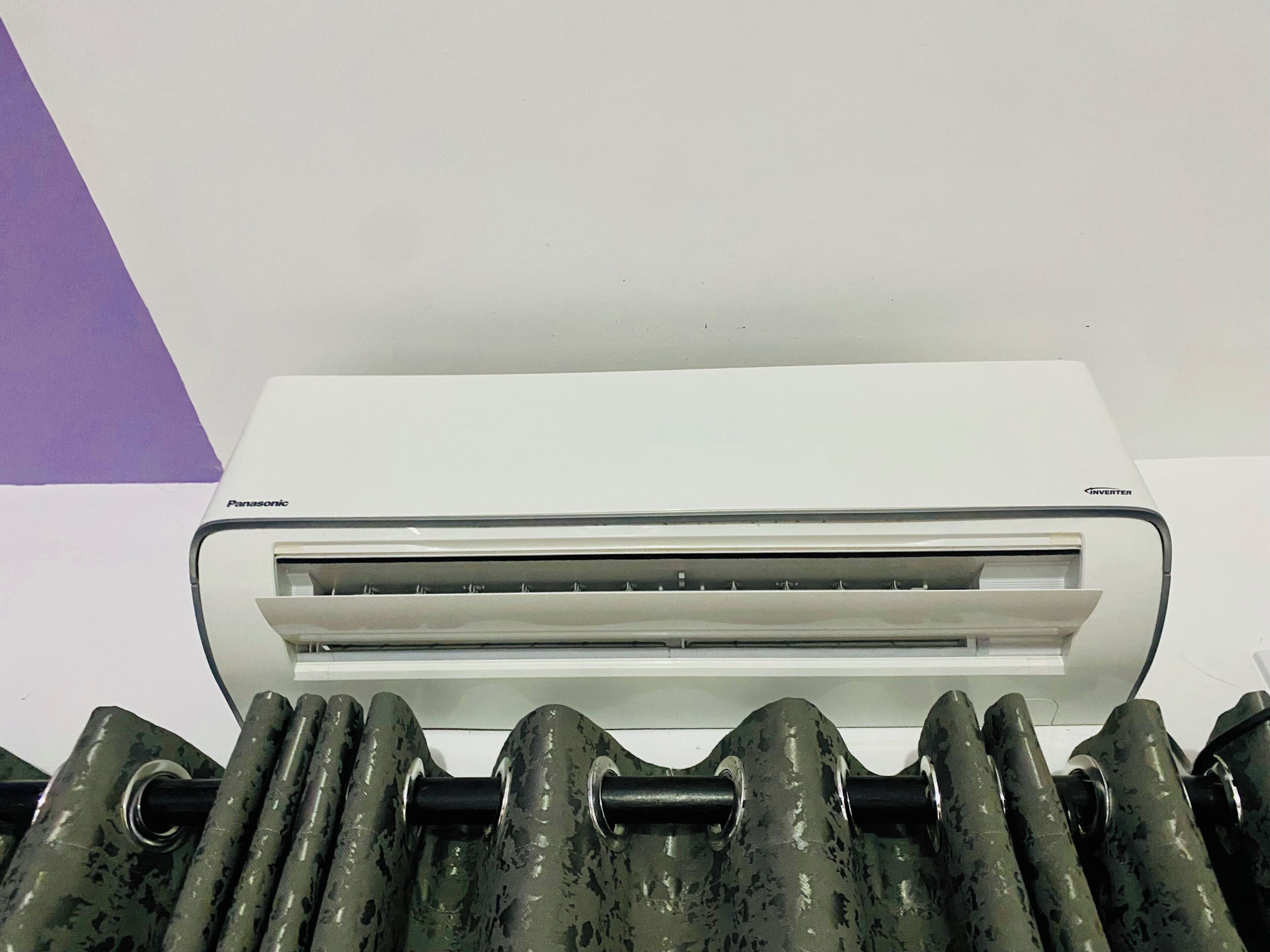 A white Panasonic air conditioner unit with an inverter feature, mounted on a wall with a purple triangular decoration.