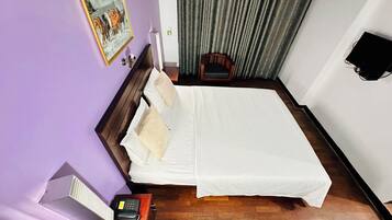 A hotel room with a bed, a chair, a desk with a telephone, a painting on the wall, and a window with curtains.