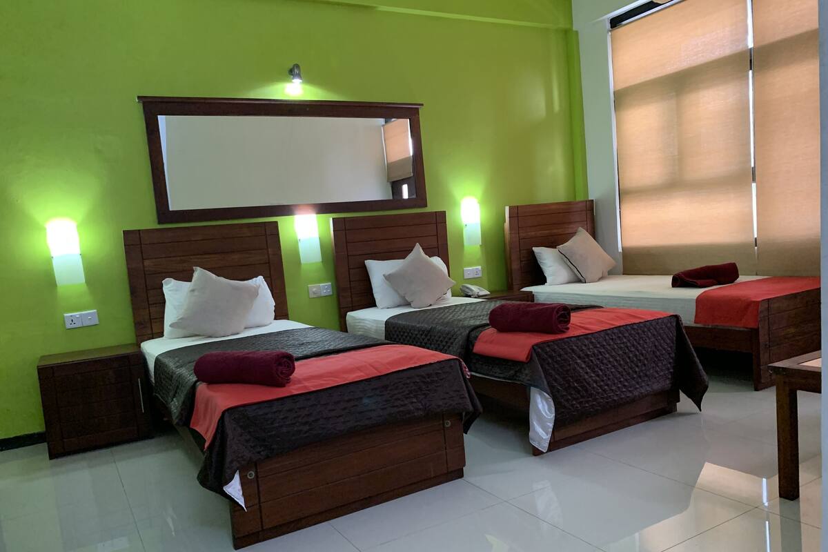A hotel room with three beds, a large mirror, and green walls.