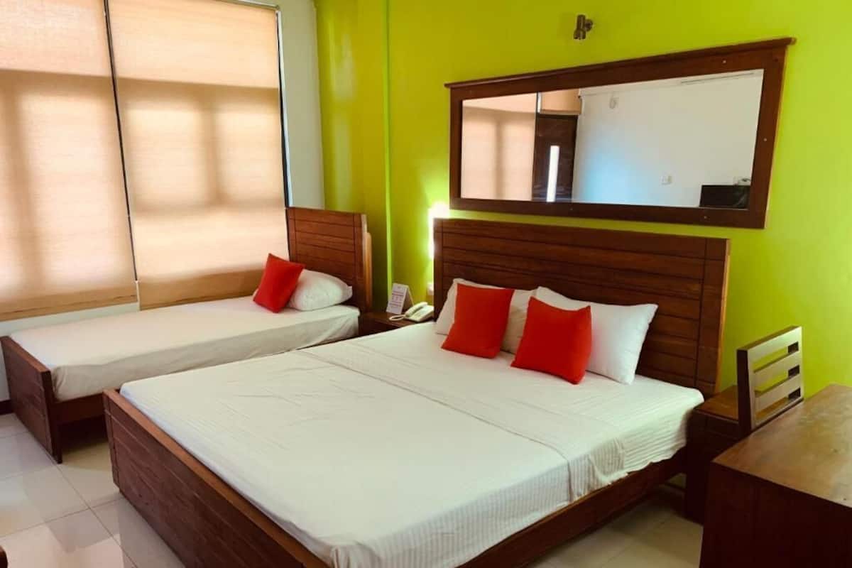 A hotel room with two beds, a wooden headboard, a bedside table, a nightstand, a mirror, and a window with blinds.