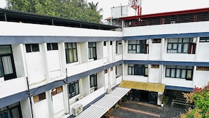 Um edifício de vários andares com telhado plano, várias janelas e uma área externa coberta com degraus que levam a uma porta.