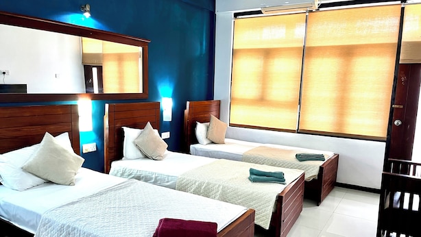 Habitación de hotel con dos camas, un ventanal grande con cortinas, cabecero de madera y un escritorio con silla.